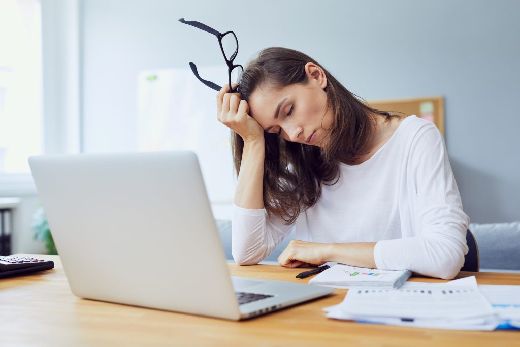 A woman feeling tired while at work, for Crown Point dental treatment turn to our skilled dentist.